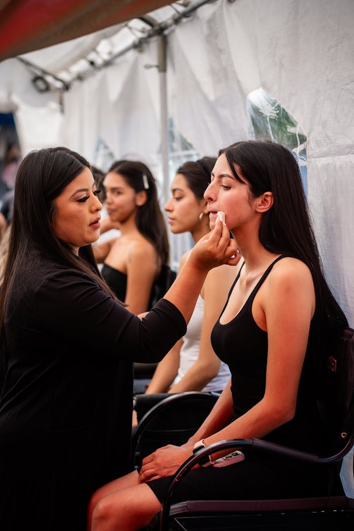 Home Makeup artist applying foundation on model in backstage setting for a fashion event.